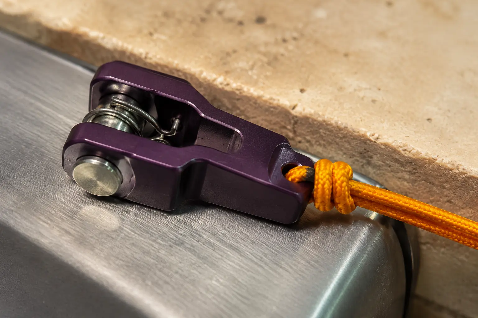 A macro view of an aubergine release latch holding a taut saffron cord